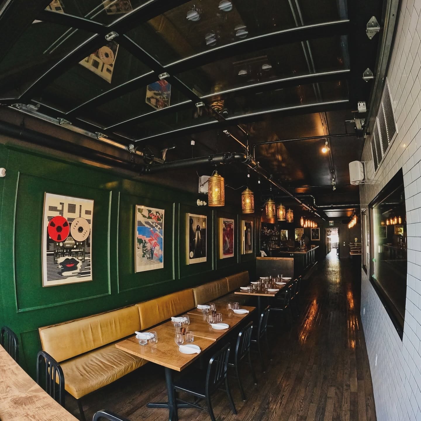 The dining room: green walls, long banquettes and framed posters under warm pendant lights